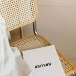 A minimalist chair with cane weaving, featuring a book titled 'Breuer'.