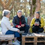 A group of senior adults playing cards together outdoors, enjoying leisure time on a sunny day.