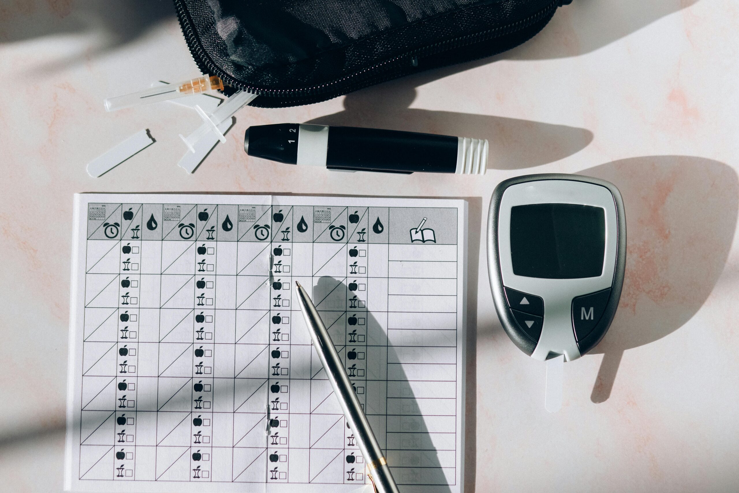 Close-up of a diabetes monitoring kit with glucometer, pen, and test strips on a table.
