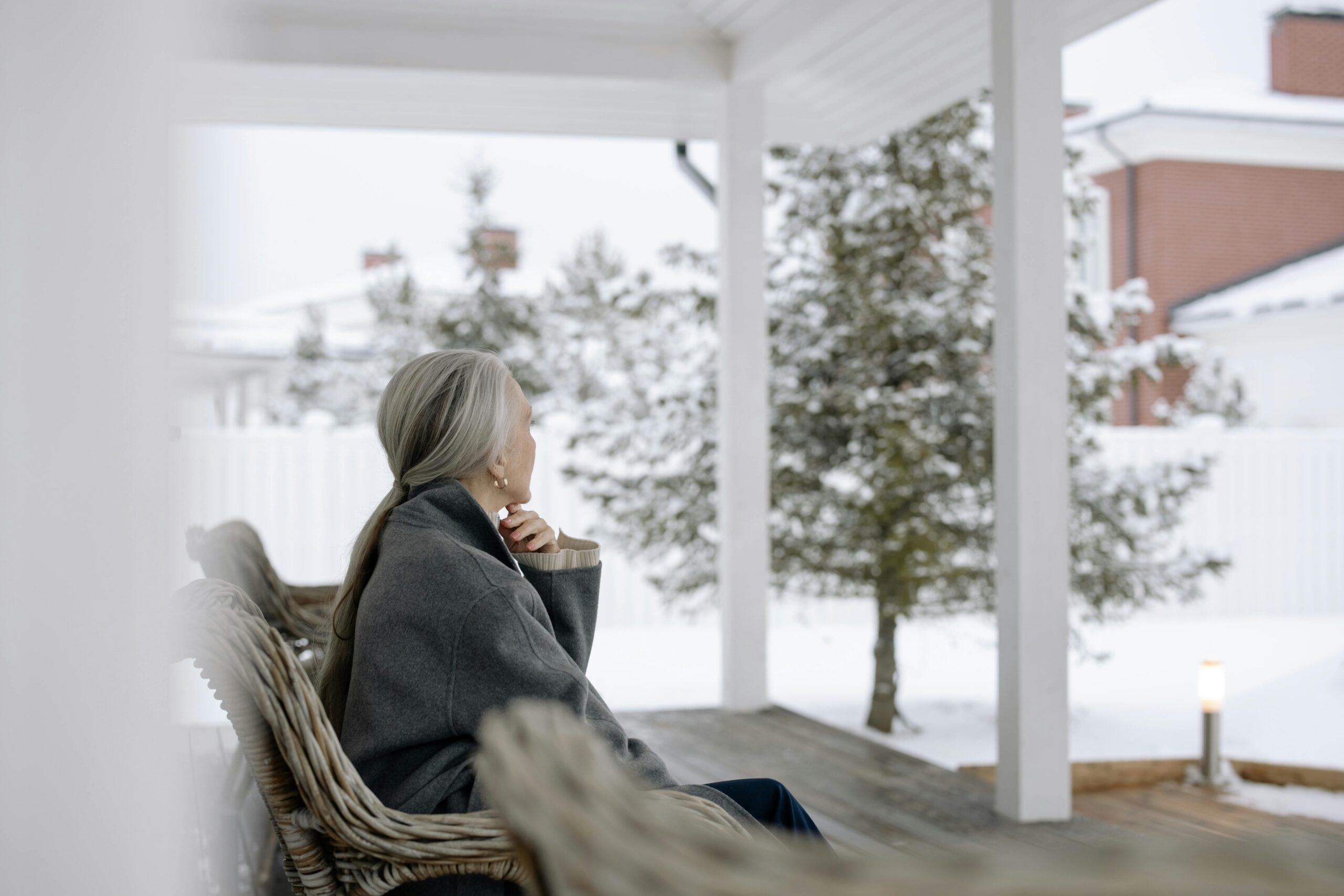 Senior woman sitting on porch in winter, enjoying serene snowy view.
